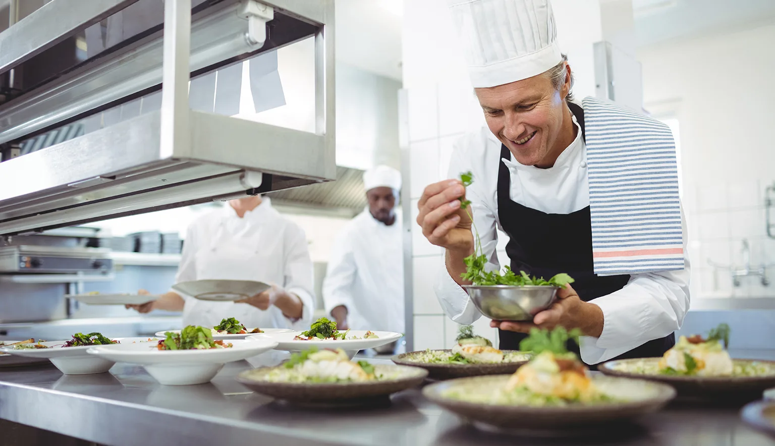 Happy chef garnishing appetizer plates at order station