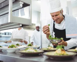 Happy chef garnishing appetizer plates at order station