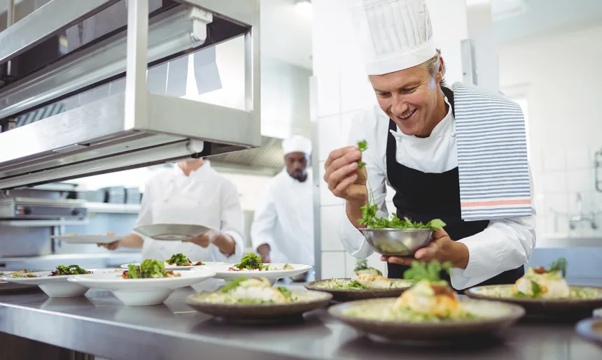 Happy chef garnishing appetizer plates at order station