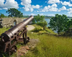 Old cannon in the fort is looking at sea with amazing clouds and island on background