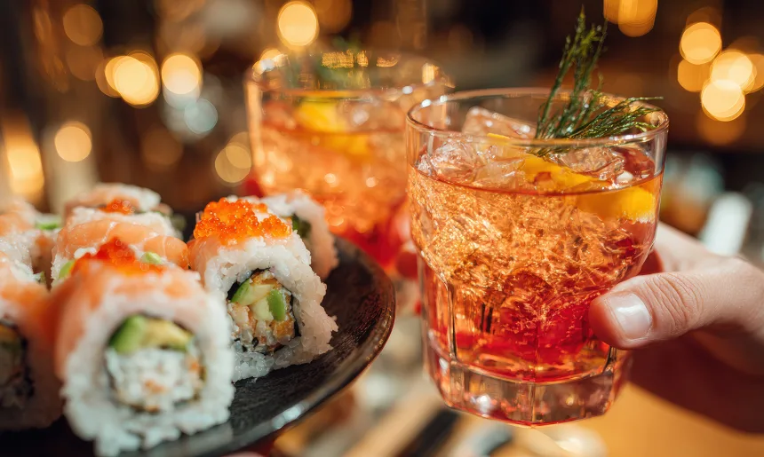 Close up of sushi rolls with salmon on plate with cocktail glass