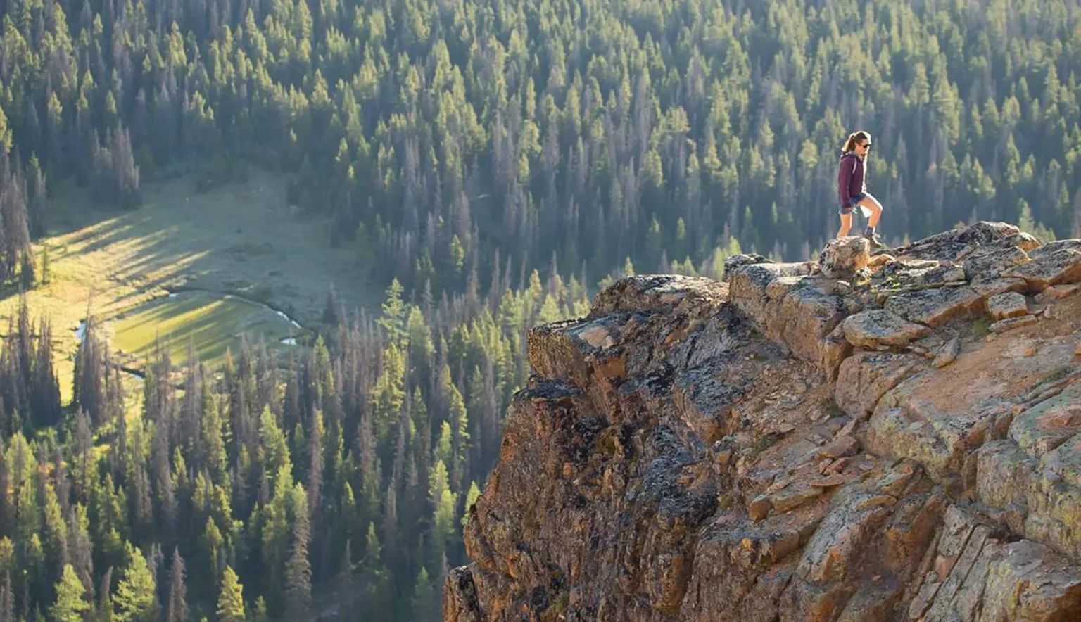 A woman hiking on a rocky ledge in Cathedral Provincial Park; lake, forest and mountains.