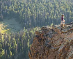 A woman hiking on a rocky ledge in Cathedral Provincial Park; lake, forest and mountains.