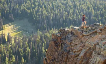 A woman hiking on a rocky ledge in Cathedral Provincial Park; lake, forest and mountains.