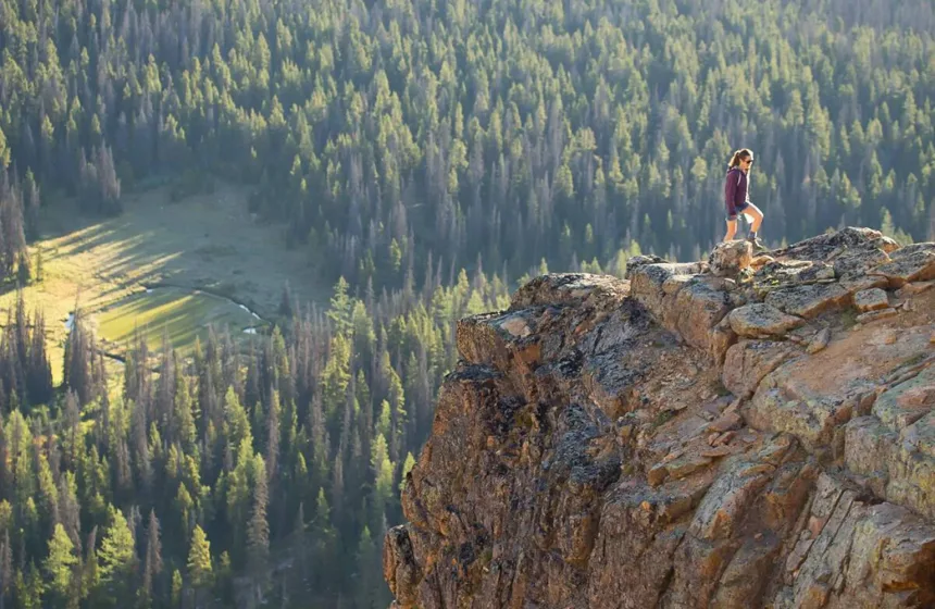 A woman hiking on a rocky ledge in Cathedral Provincial Park; lake, forest and mountains.