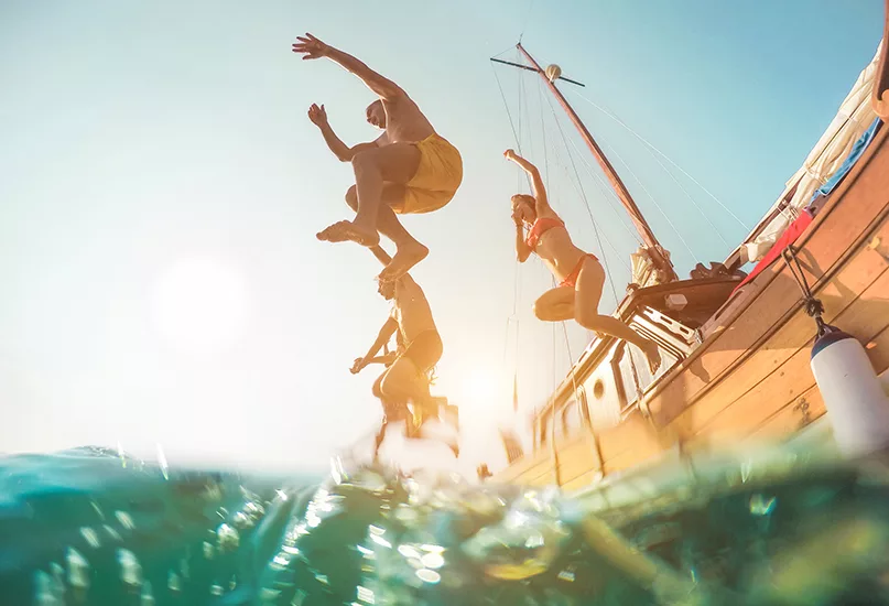 Happy friends diving from sailing boat into the sea